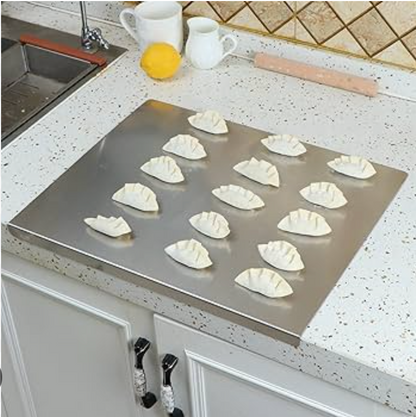 Planche à découper en inox avec rebord anti-débordement présentant des raviolis préparés dans une cuisine moderne