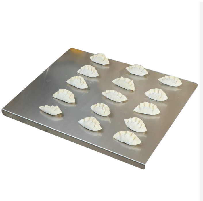 Planche à découper en inox avec rebord présentant des raviolis disposés, vue en angle sur fond blanc